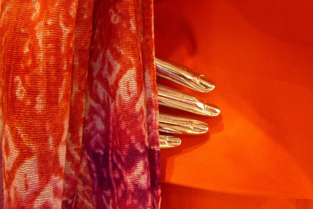 Draped orange patterned fabric and a metallic mannequin hand