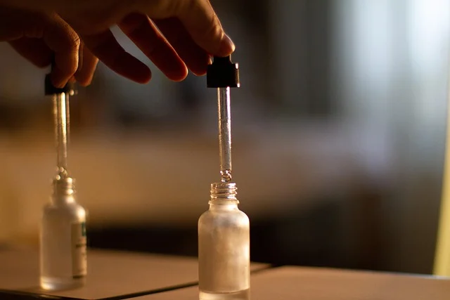 A hand holding a dropper above a small glass oil bottle