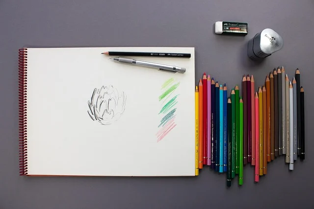 A sketchbook, colored pencils, and drawing tools laid out